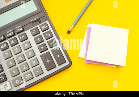 Modern calculator and pencil with stickers for notes on a yellow background, top view Stock Photo