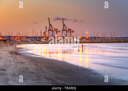 Cranes at sunset with sandy beach and reflections in the foreground at  Larnaca port, Cyprus island. Stock Photo