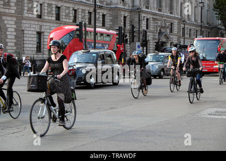 Office workers cycling home from work ride bikes through traffic junction near Houses of Parliament in Central London England UK GB   KATHY DEWITT Stock Photo
