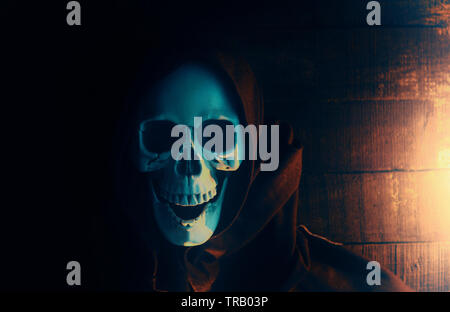 Halloween costume ghost scary skeleton wearing a hooded coat / Grim reaper with skull in black hood on the dark Stock Photo