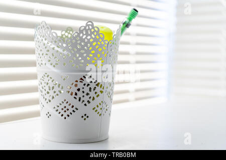 Decorative container used as a pencil holder in a home office, against a window, with sunbeams and white home decor. Stock Photo