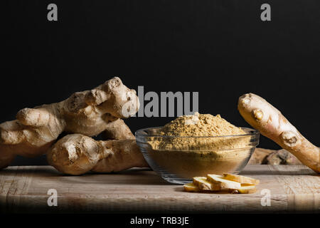 Ginger powder in glass bowl on wooden cutting board with ginger roots and slices. Healthy eating concept. Stock Photo