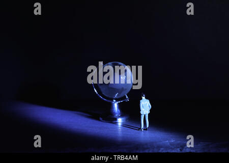 Miniature man looking at Small crystal globe in front of dark and dramatic light.global issues concept Stock Photo
