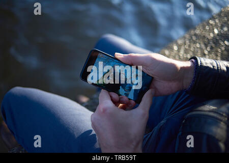 Caucasian man sitting outside in the back garden of a pub along the water using his mobile phone in the city centre of Amsterdam Stock Photo