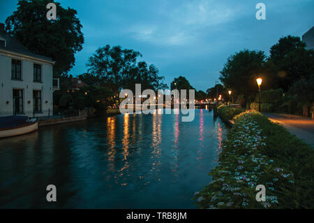 Night view of wide tree-lined canal, bridge and lamp post lighting at Weesp. Pleasant village full of canals and green in Netherlands. Stock Photo