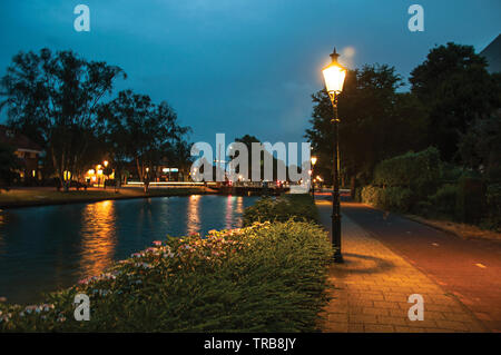 Night view of wide tree-lined canal, bridge and lamp post light in the foreground at Weesp. Pleasant village full of canals and green in Netherlands. Stock Photo