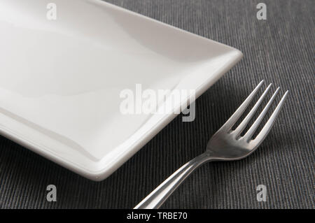 Square ceramic plate and a fork on a table Stock Photo
