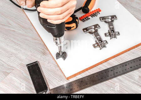 Man drills holes for installation of furniture hinges for facade of kitchen. Stock Photo