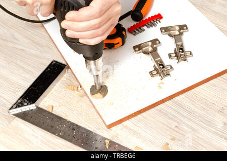 Man drills holes for installation of furniture hinges for facade of kitchen. Stock Photo