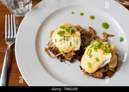 Pulled pork served on fried potato pancakes topped with poached egg and garnished with hollandaise sauce and fresh green onion aka 'farmers Benedict' Stock Photo