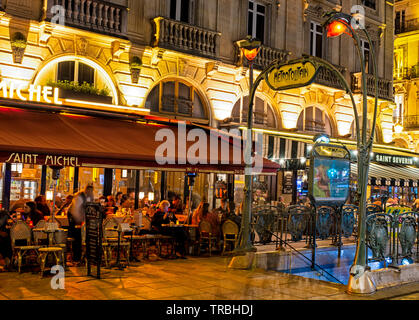 Entrance to the Metropolitain subway on Rue St. Michel in the evening with a view of restaurants and people dining outdoors. Stock Photo