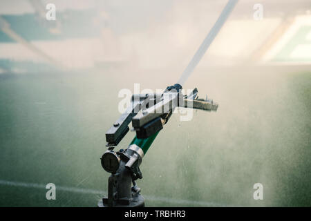 Automatic water irrigator in action. Close-up sprinkler of automatic watering. Green grass soccer field Stock Photo