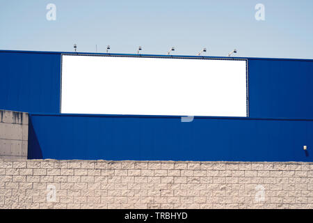 Blank advertising billboard in metallic frame with spotlight on blue building or outside department store building in the city with blue sky backgroun Stock Photo
