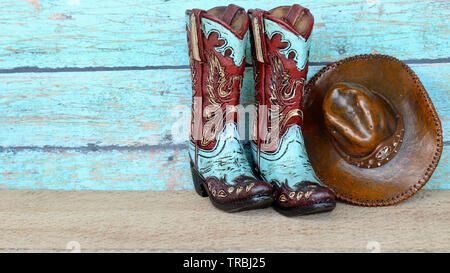 pair of colorful teal and brown cowboy boots and hat standing on natural wood with a teal wooden background Stock Photo