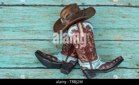 Brown and teal cowboy boots and hat laying on a teal wood background Stock Photo