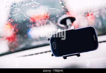 Smart phone on holder, rainy weather seen through wind shield, cellphone with black mock up blank on screen. Advertisement for traffic and navigation Stock Photo