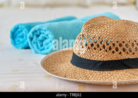 Beach holidays accessories close up. Woman straw hat on foreground, folded two blue color towels lie on bed, no people. Concept image of summer season Stock Photo