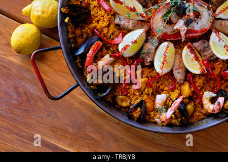 Delicious Spanish seafood paella, view from above. Cooked with sturgeon halibut fillet, peeled shrimps squids, mussels and lobster decorated with lemo Stock Photo