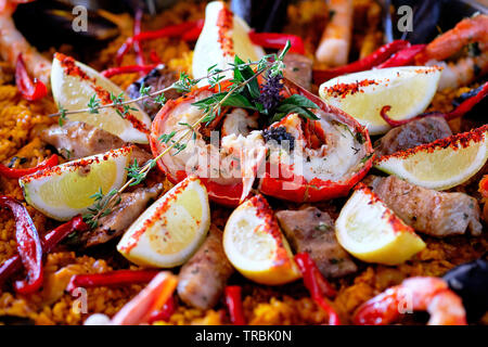 Close up above top view image of ripe ingredients of prepared served paella spanish traditional cuisine, bright colors. Dish garnished with lemon slic Stock Photo