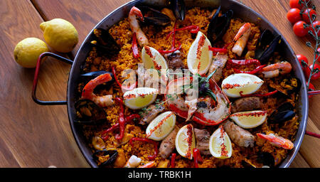 Delicious Spanish seafood paella, view from top. Cooked with sturgeon halibut fillet, peeled shrimps squids, mussels and lobster decorated with lemon Stock Photo