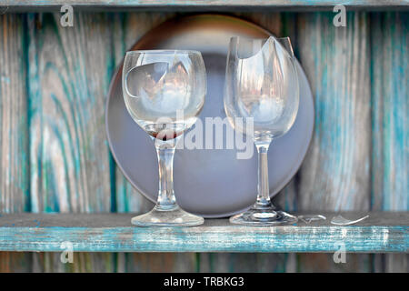 Two broken wine glasses placed on a wooden shelf Stock Photo