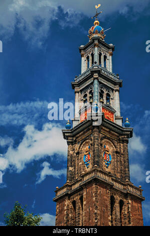 Pointed bell tower church made of bricks and golden clock in Amsterdam. City with huge cultural activity, canals and bridges in Netherlands. Stock Photo