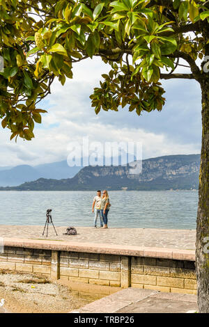 BARDOLINO, LAKE GARDA, ITALY - SEPTEMBER 2018: Man and woman taking a picture of themselves on the edge of Lake Garda. Stock Photo