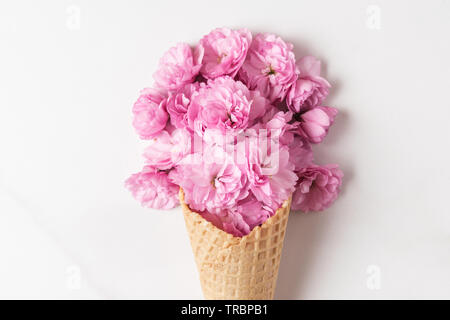 pink cherry blossoming flowers bouquet in ice cream cone on white background. wedding or holiday background. Flat lay. top view. close up Stock Photo