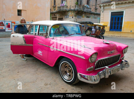 Colourful pink Classic American car picking up taxi passenger on a street  in the  Old Town or Havana Vieja, Havana, Cuba, Caribbean