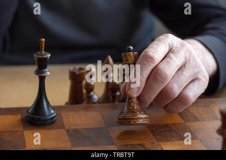 The hand of an old man puts a black king's figure on the board acknowledging loss, concept business games, selective focus, copyspace Stock Photo