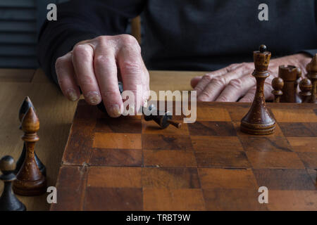 The hand of an old man puts a black king's figure on the board acknowledging loss, concept business games, selective focus, copyspace Stock Photo
