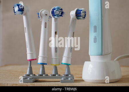 Four well-used electric toothbrush heads on a home-made Lego stand, next to a Braun electric toothbrush on its wireless rechargeable base. Stock Photo