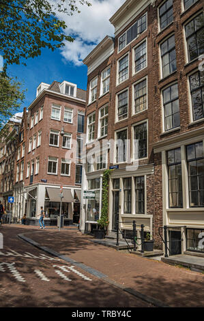 Street with old brick buildings, shops and people passing by in Amsterdam. City with huge cultural activity, canals and bridges in Netherlands. Stock Photo