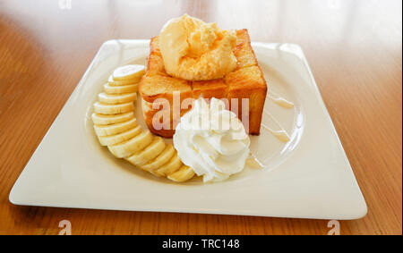 Dessert bread honey santos vanilla ice cream with whip cream banana fruit and honey bee on white plate in the cafe coffee shop Stock Photo