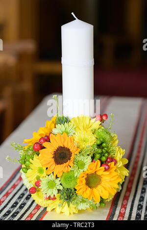 Baptismal candle decorated with a round sunflower bouquet, in preparation for the baptism, first of seven Sacraments in the Orthodox Christian Church Stock Photo