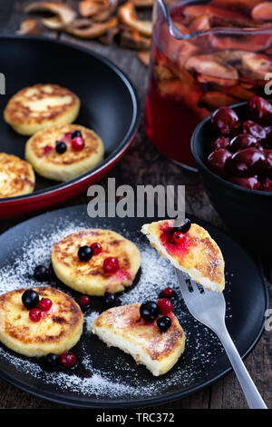 Cottage cheese pancakes on a black plate with cream, jam and cup of ...