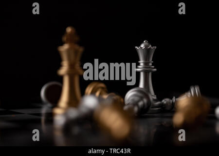 Queen and king standing in the midst of falling chess on board Stock Photo