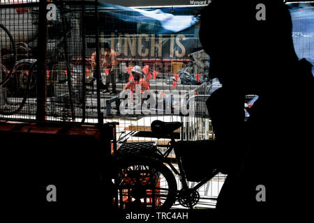 An office worker, in silhouette  passes the Light Rail construction in Sydney, Australia. Workers are in hard hats . A bicycle is in the foreground Stock Photo