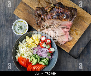 Delicious Lamb leg roast cooked on a rotisserie served with fresh greek salad and sauce for souvlaki wraps. Stock Photo