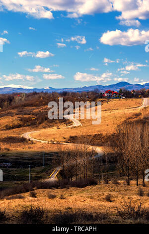 winding road thru hills in early spring time and snow covered mountain peaks in the far background Stock Photo