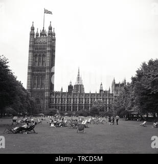 1960s, historical, view across Victoria Tower gardens with people in deckchairs sitting on the grass, Westminster, London, England, UK. The Union Jack flag is flying on top of the tower, which is located beside the Palace of Westminster. Stock Photo