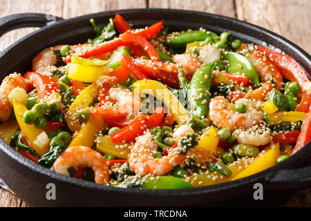 Roasted shrimps with peppers, onions, herbs, pod peas, sesame close-up in a frying pan on the table. horizontal Stock Photo