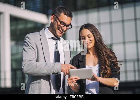 Business colleagues are using digital tablet outside the company building. Stock Photo