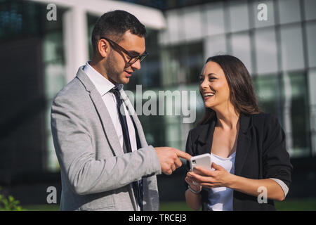 Business colleagues are using smartphone outside the company building. Stock Photo