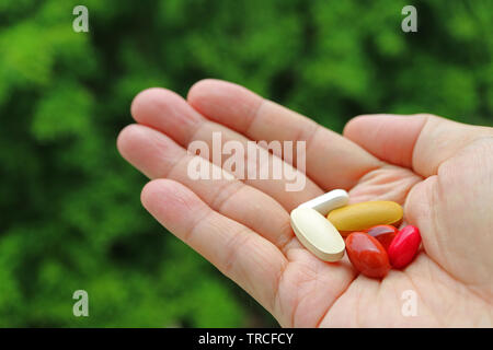 Assorted Supplement Pills in Man's Palm with Blurry Green Foliage in Background Stock Photo
