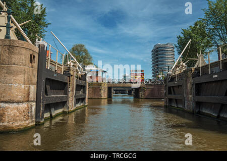 Open canal sluice gate, bridge and building under sunny blue sky in Amsterdam. City with huge cultural activity, canals and bridges in Netherlands. Stock Photo