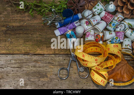 Spools of thread and basic sewing tools including pins, needle, a thimble, and tape measure on an old wooden tabletop. concept with copy space. Stock Photo