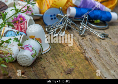 Spools of thread and basic sewing tools including pins, needle, a thimble, and tape measure on an old wooden tabletop. concept with copy space. Stock Photo