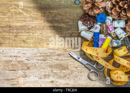 Spools of thread and basic sewing tools including pins, needle, a thimble, and tape measure on an old wooden tabletop. concept with copy space. Stock Photo