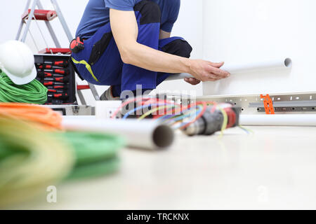 electrician at work with the plastic pipe in his hand to pass the electric cables to the sockets, electrical wiring Stock Photo